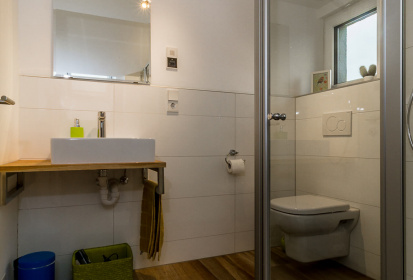 Blick ins Badezimmer mit Bodenfliesen in Holzoptik, Waschtisch aus Holz und Toilette.jpg