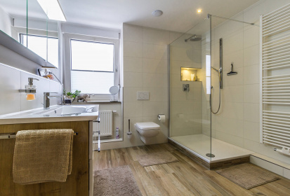 ein helles, freundliches Bad mit Bodenfliesen in Holzoptik und begehbarer Dusche.jpg