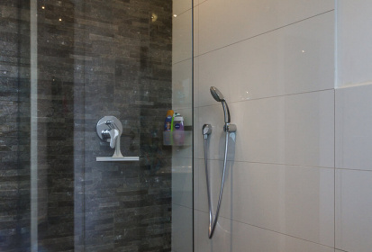 Blick in die verglaste ebenerdige Dusche mit durchgehenden Fliesen und Mosaikfliesen an einer Wand.jpg