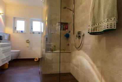Begehbare Dusche mit abgerundeter Verglasung, Fliesen durchgezogen und Abfluss der Dusche in der Wand.jpg
