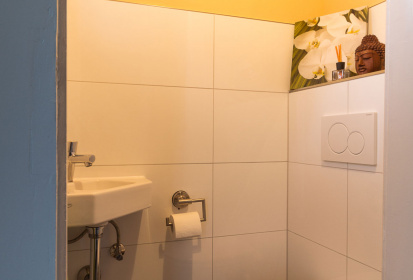 Blick ins Gaeste WC mit Toilette, Eckwaschbecken, weiss gefliest und gelb gestrichen.jpg